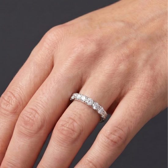 Close-up of a hand resting against a dark gray background, wearing a thick white metal band featuring a row of large, round-cut diamonds.