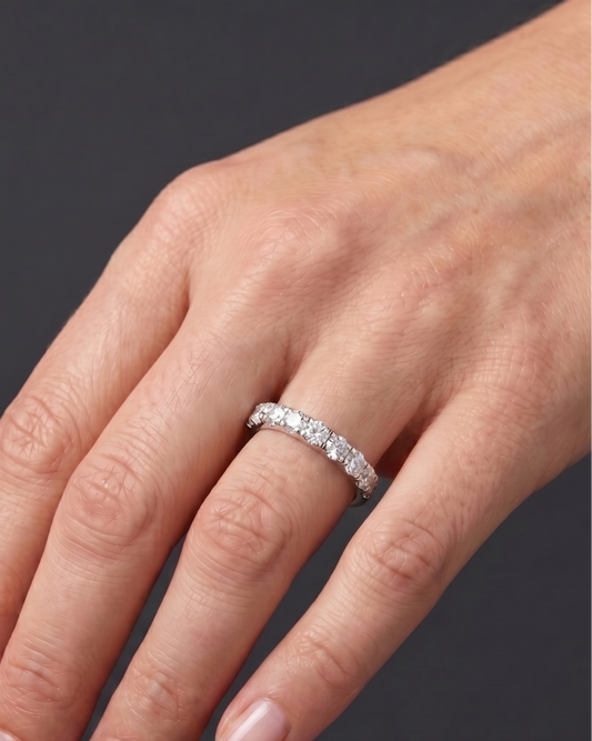 Close-up of a hand resting against a dark gray background, wearing a thick white metal band featuring a row of large, round-cut diamonds.