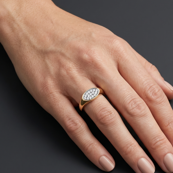 Lifestyle view of a model wearing a modern 14k yellow gold pinky signet ring featuring a flat oval face encrusted with micro-pavé white diamonds.