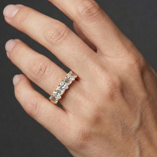 A top-down view of a 14K yellow gold eternity ring with a continuous line of bold, horizontally-set emerald-cut diamonds on a hand.