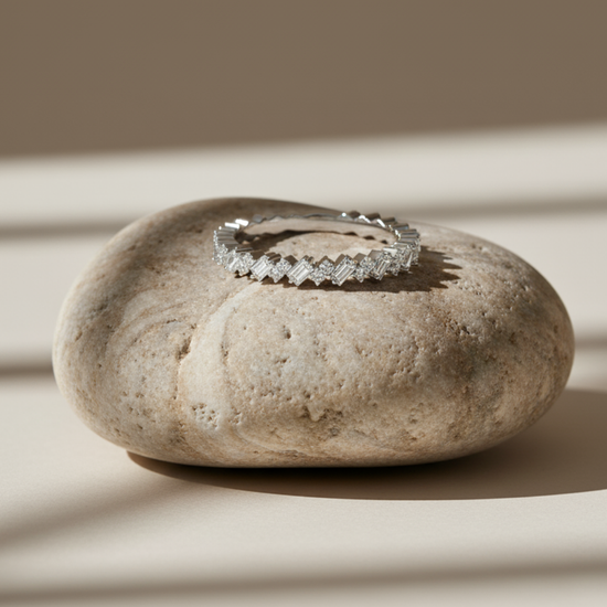 A close-up view of a 14K yellow gold band ring with an alternating pattern of baguette and round diamonds on a beige stone.