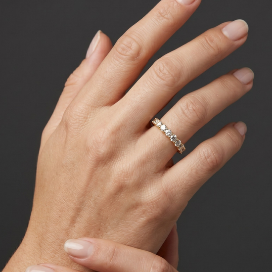 Close-up of a woman's hand wearing a yellow gold diamond eternity band against a dark gray background.