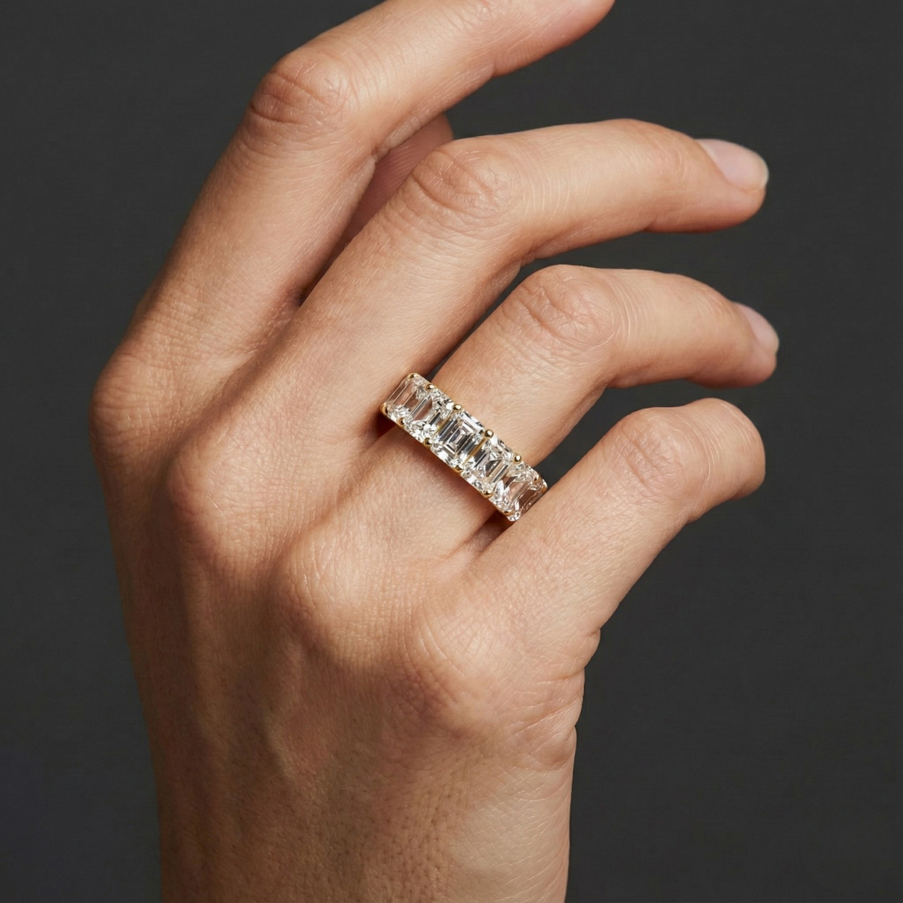 A top-down view of a 14K yellow gold wide-band ring with five horizontally set emerald-cut diamonds on hand.