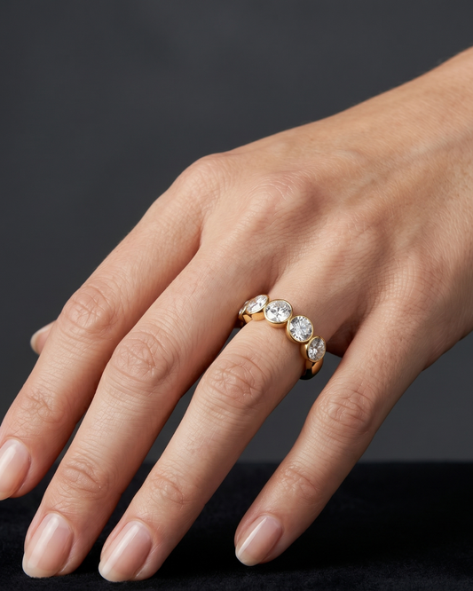 Close-up of a hand resting on a black surface, wearing a thick gold band featuring a row of five round, bezel-set diamonds.