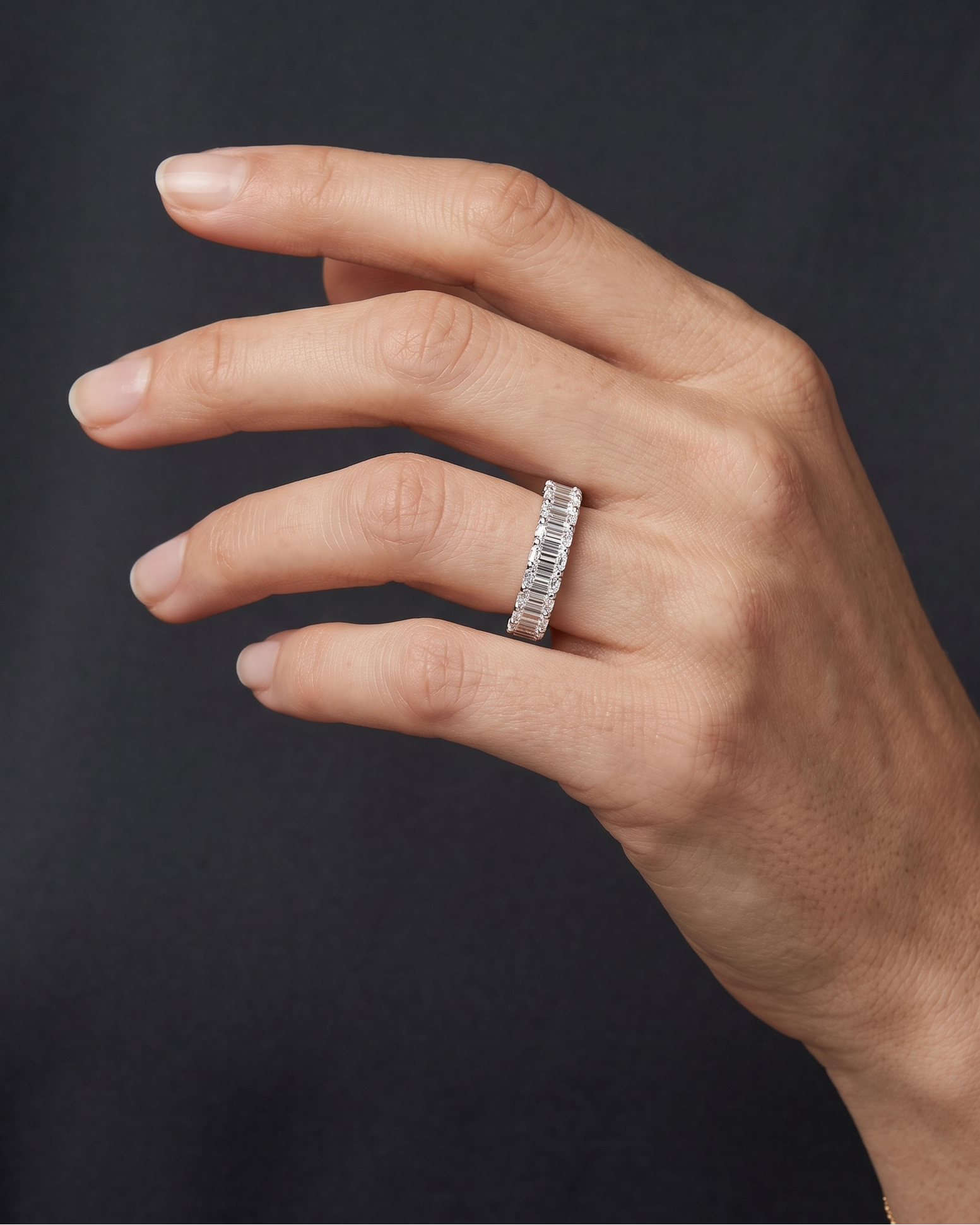 Lifestyle view of a model wearing a heavy-carat 14k yellow gold eternity ring featuring exceptionally large, vertically set emerald-cut diamonds.
