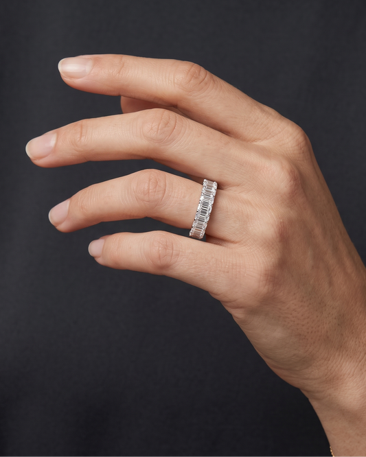 Lifestyle view of a model wearing a heavy-carat 14k yellow gold eternity ring featuring exceptionally large, vertically set emerald-cut diamonds.
