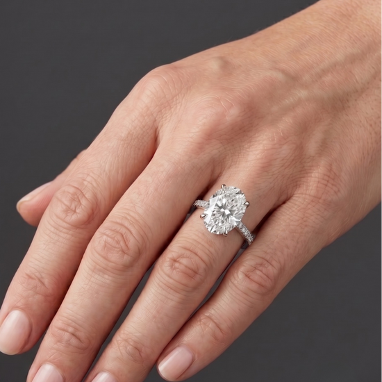 Elegant white gold engagement ring featuring a large oval-cut center diamond and a pavé diamond band, worn on a woman's hand.