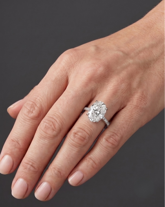 Elegant white gold engagement ring featuring a large oval-cut center diamond and a pavé diamond band, worn on a woman's hand.