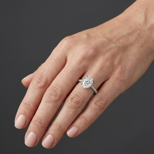 Elegant white gold engagement ring featuring a large oval-cut center diamond and a pavé diamond band, worn on a woman's hand.