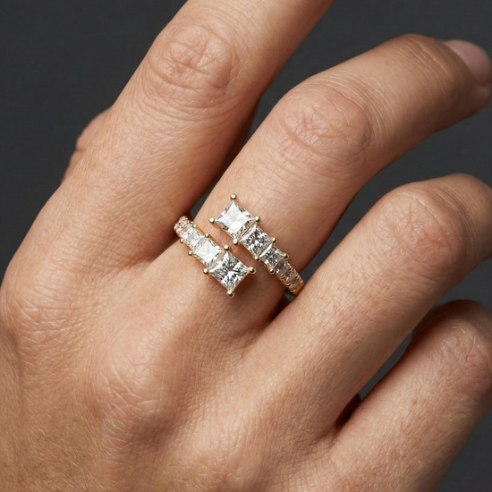 Close-up of a hand wearing a 14k yellow gold open diamond ring featuring princess-cut diamonds set across a modern, split-band design, photographed against a dark background to highlight clean lines, refined sparkle, and contemporary elegance.