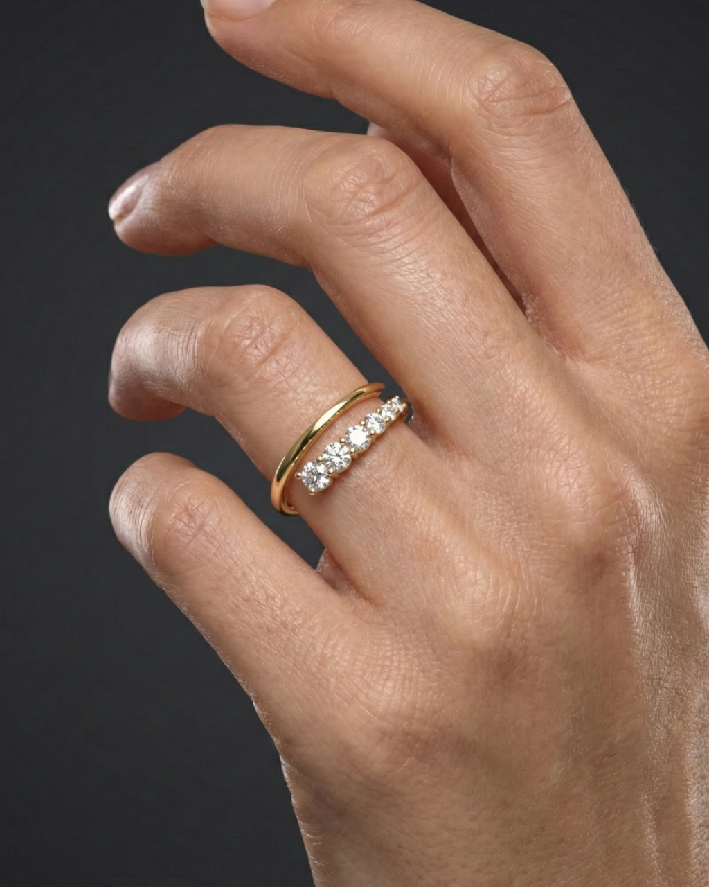 Close-up of a hand wearing a 14k yellow gold diamond band featuring a row of round brilliant-cut diamonds set across a slim polished band, photographed against a dark background to highlight delicate sparkle and timeless elegance.