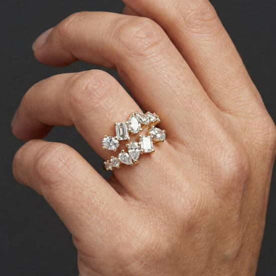 Close-up of a hand wearing a 14k yellow gold diamond statement ring featuring a clustered arrangement of mixed-cut diamonds, photographed against a dark background to emphasize dimensional sparkle, modern design, and elevated craftsmanship.