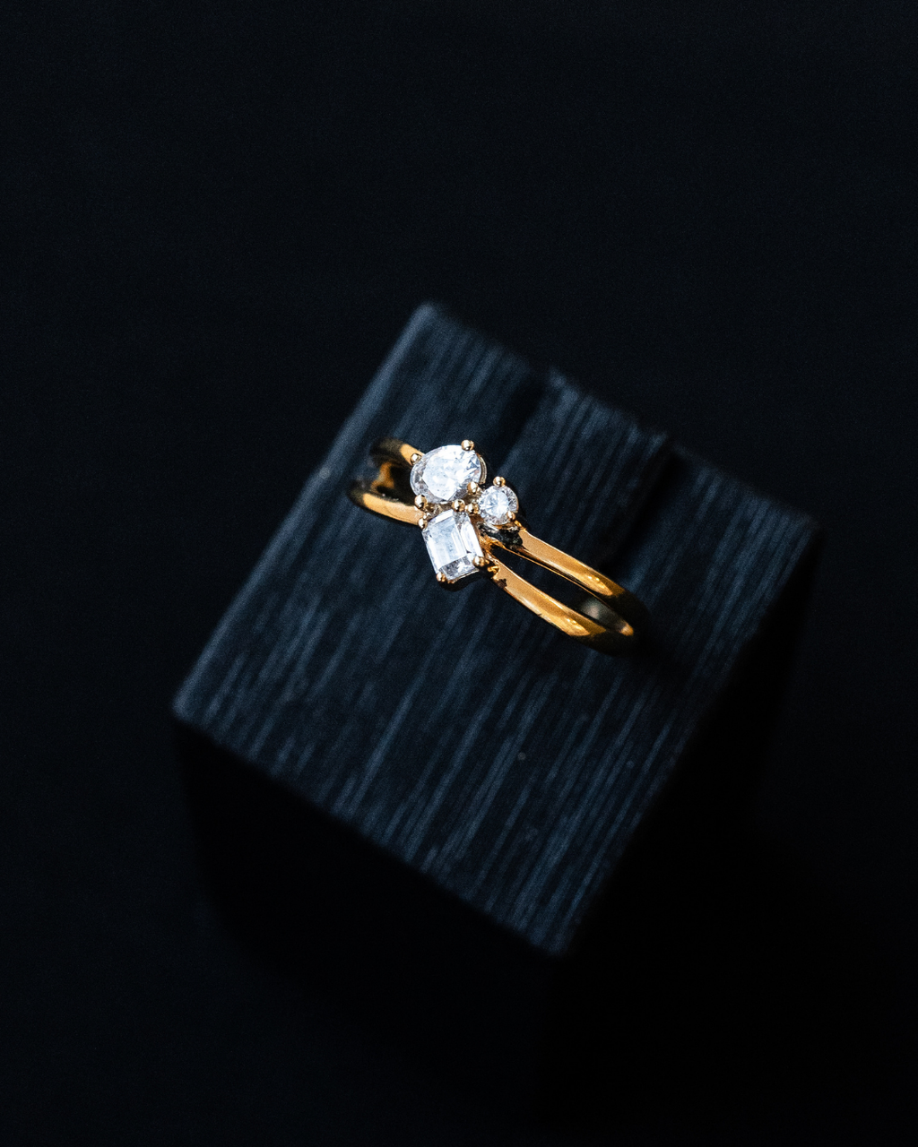 Yellow gold architectural diamond cluster ring featuring mixed-cut diamonds, resting on a black textured display block.