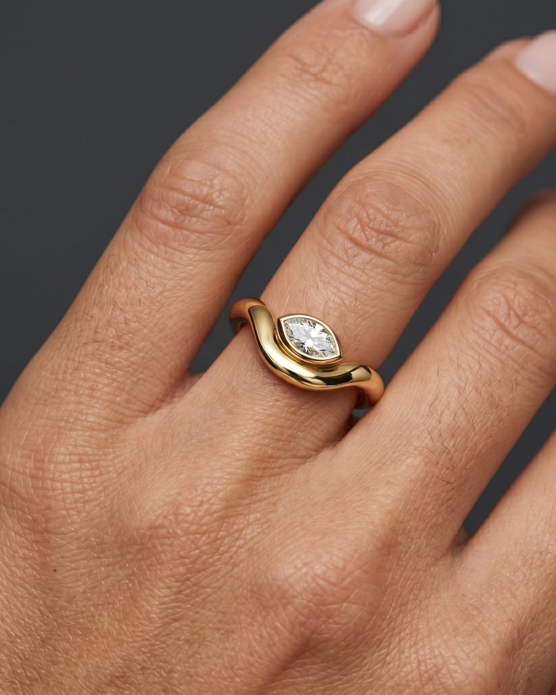 Close-up lifestyle view of a modern 14k yellow gold ring featuring a horizontally set marquise-cut diamond in a sleek bezel setting on a fluid, wavy comfort-fit band.