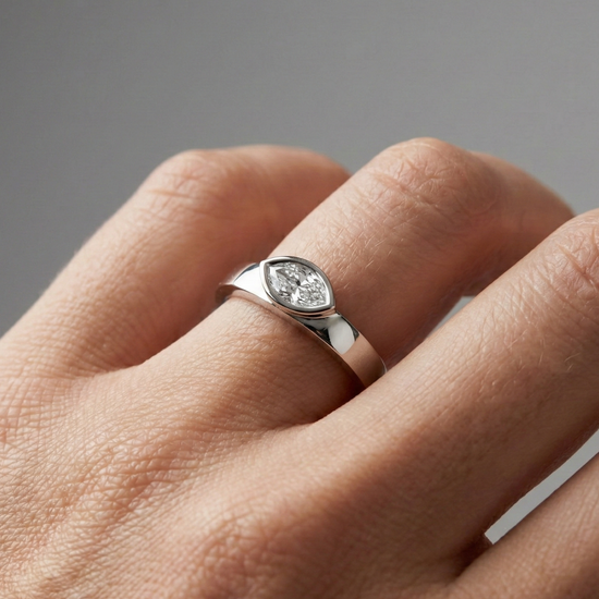 A top-down view of a 14K white gold bypass ring with a single, horizontally-set oval diamond in a bezel setting on hand.