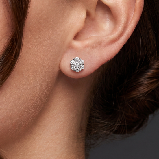 A close-up of a model's ear wearing a small, round cluster stud earring set with clear gemstones in a silver-toned metal.