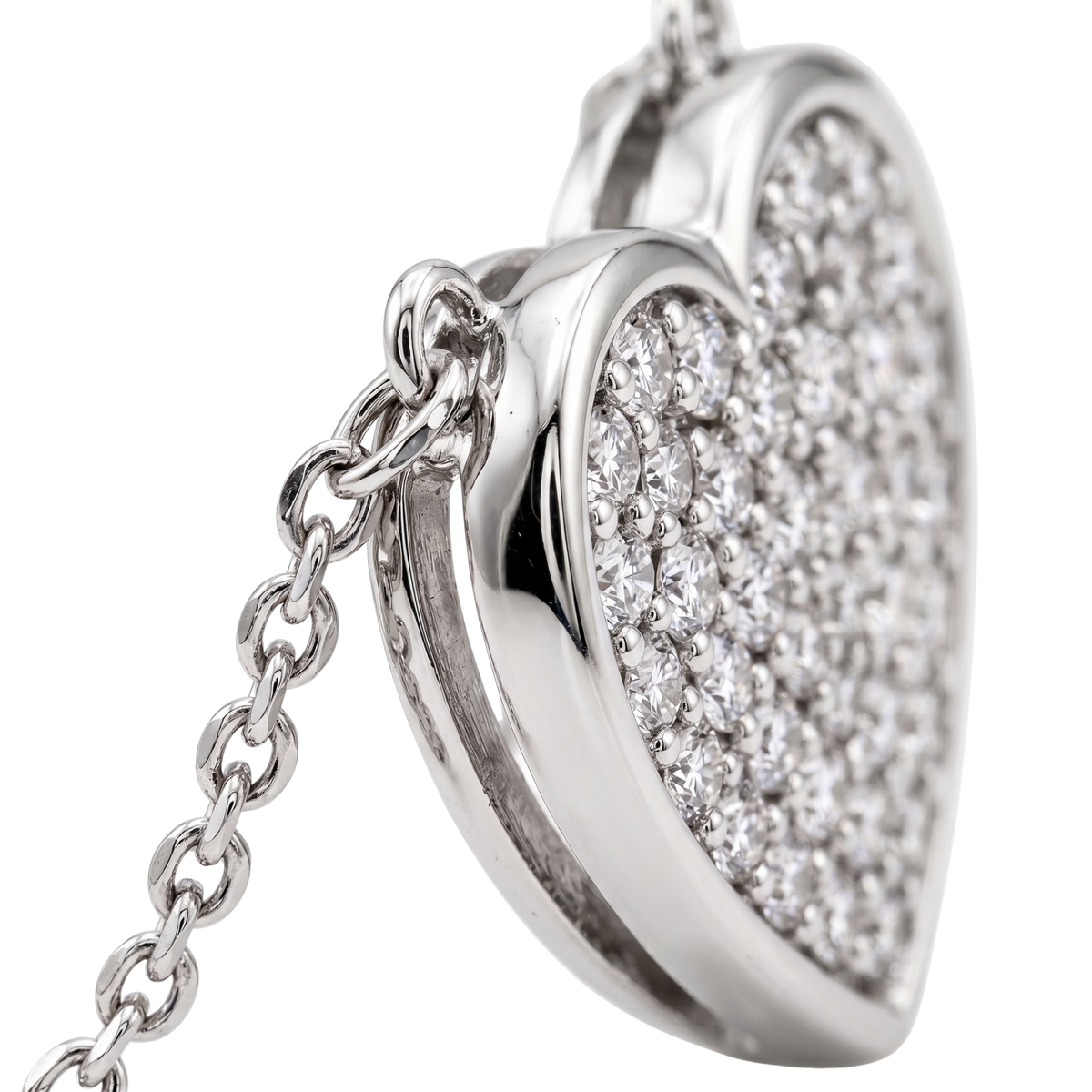 A close-up of a silver heart-shaped pendant necklace, partially open to reveal a heart-shaped locket filled with pavé-set clear gemstones, attached to a silver chain against a white background.