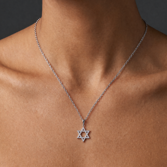 A close-up of a model's neck and upper chest wearing a delicate silver chain necklace with a Star of David pendant.