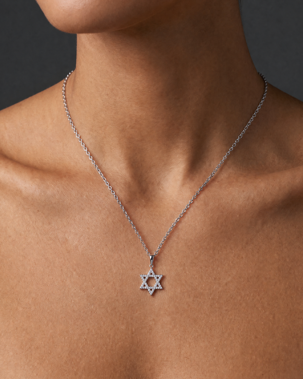 A close-up of a model's neck and upper chest wearing a delicate silver chain necklace with a Star of David pendant.