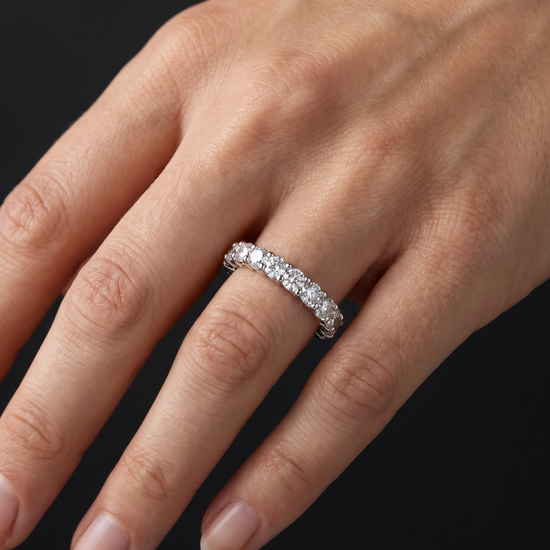 A close-up of a hand wearing a silver diamond eternity ring against a solid black background.