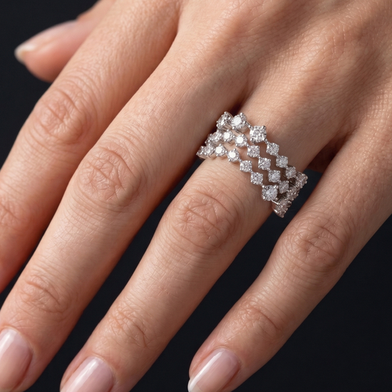 A close-up of a hand wearing a silver-toned diamond ring with a repeating geometric diamond pattern, set against a solid black background.