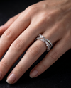 A close-up of a hand wearing three silver rings, including a diamond band and two stacked eternity-style bands, against a dark background.