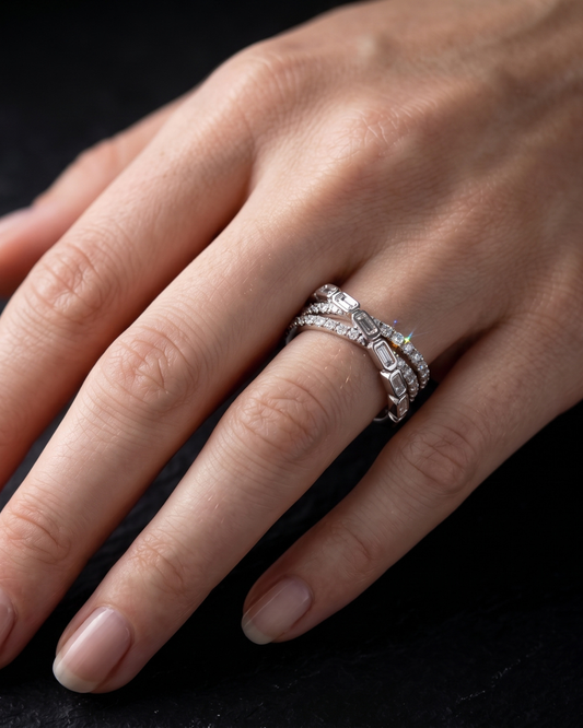 A close-up of a hand wearing three silver rings, including a diamond band and two stacked eternity-style bands, against a dark background.
