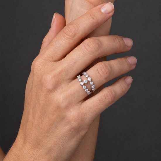 A close-up of a person's hand wearing two delicate silver band rings set with small clear stones, against a dark gray background.