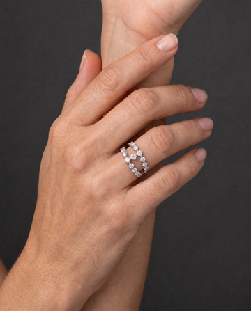 A close-up of a person's hand wearing two delicate silver band rings set with small clear stones, against a dark gray background.