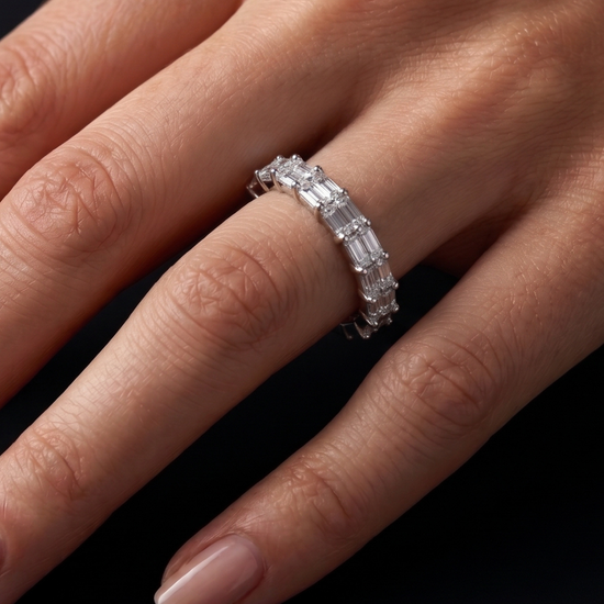 A close-up of a hand wearing a silver band ring set with baguette-cut clear gemstones against a dark background.