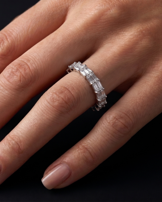 A close-up of a hand wearing a silver band ring set with baguette-cut clear gemstones against a dark background.