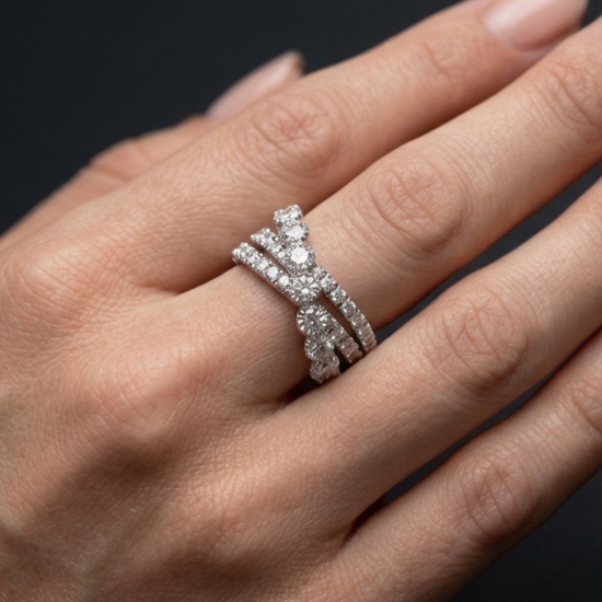 A close-up of a hand wearing a silver-toned triple-band ring set with sparkling clear gemstones, against a dark background.
