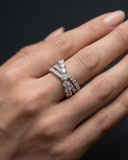 A close-up of a hand wearing a silver-toned triple-band ring set with sparkling clear gemstones, against a dark background.