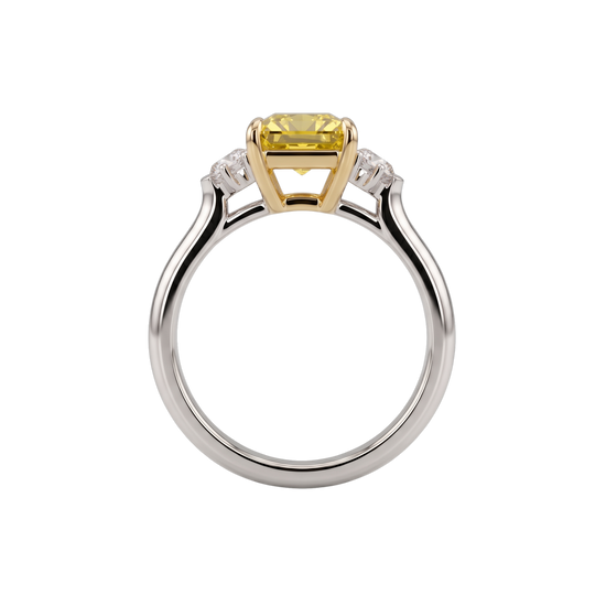 A profile view of an engagement ring showing the full circular white metal band and the side of the setting against a black background. The center stone is a pastel yellow emerald-cut diamond resting in an elevated yellow gold basket setting with an open gallery. Clear white side diamonds are visible sloping down the shoulders of the band.