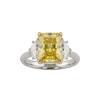 A top-down view of a three-stone engagement ring against a solid black background. The center features a large, pastel yellow emerald-cut diamond set in four yellow gold prongs. It is flanked by two smaller, clear white diamond side stones. The band of the ring is a smooth, polished white metal.
