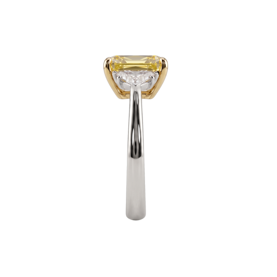 A straight-on side view of an engagement ring resting vertically against a black background, showcasing the height and profile of the setting. At the top, the edge of a pastel yellow center diamond is visible within a yellow gold setting. The smooth white metal band sweeps upward to support the setting, partially revealing the side profile of a clear accent diamond.