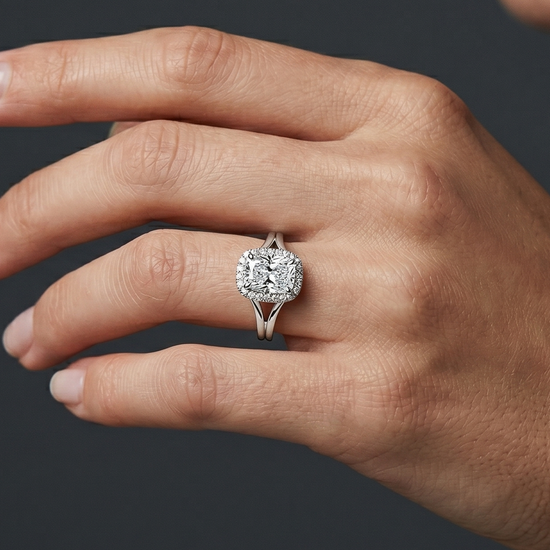 A close-up of a woman's hand wearing a sparkling elongated cushion-cut diamond ring with a split-shank setting against a dark gray background.