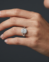 A close-up of a woman's hand wearing a sparkling elongated cushion-cut diamond ring with a split-shank setting against a dark gray background.