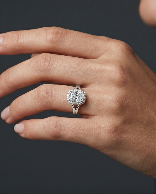 A close-up of a woman's hand wearing a sparkling elongated cushion-cut diamond ring with a split-shank setting against a dark gray background.
