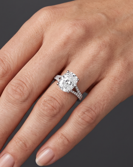 Close-up of a woman's hand elegantly posed against a dark charcoal gray background, wearing a white gold or platinum engagement ring with a large cushion-cut diamond and a sparkling split-shank band.