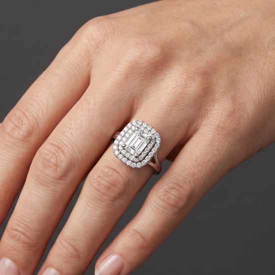 Close-up of a woman's hand resting gracefully against a dark charcoal gray background, wearing a large diamond engagement ring. The ring features an emerald-cut center stone surrounded by a double halo of smaller diamonds.