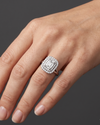 Close-up of a woman's hand resting gracefully against a dark charcoal gray background, wearing a large diamond engagement ring. The ring features an emerald-cut center stone surrounded by a double halo of smaller diamonds.