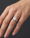 Close-up of a woman's hand wearing an emerald-cut diamond engagement ring with a split-shank band against a dark charcoal gray background.