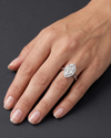 A close-up of an elegant woman's hand resting on a dark charcoal gray surface. She is wearing a brilliant marquise-cut diamond engagement ring with a diamond halo on her ring finger. Soft, diffused lighting highlights the sparkling gemstone, the polished silver band, and the natural texture of her skin.