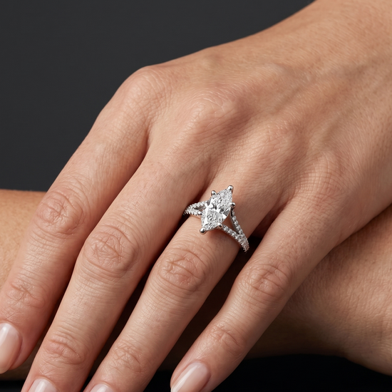 A close-up of a woman's hand wearing a marquise-cut diamond engagement ring with a pave split-shank band, set against a dark gray background.