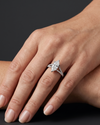 A close-up of a woman's hand wearing a marquise-cut diamond engagement ring with a pave split-shank band, set against a dark gray background.