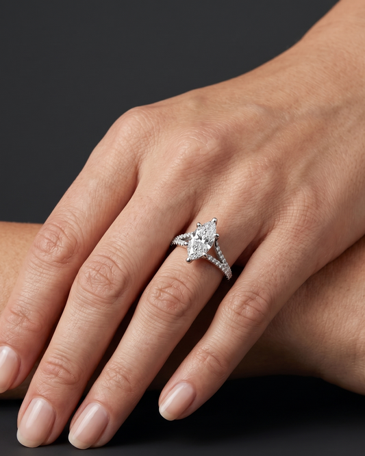 A close-up of a woman's hand wearing a marquise-cut diamond engagement ring with a pave split-shank band, set against a dark gray background.
