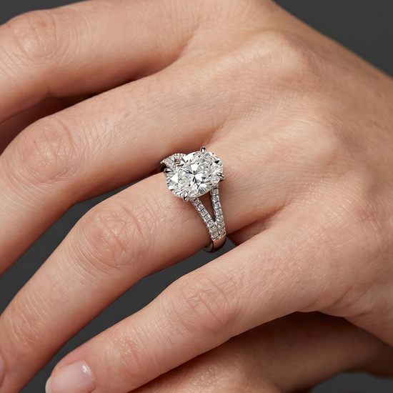 A close-up, hyper-realistic editorial photograph of a woman's hands gracefully posed against a smooth, dark charcoal gray background. On her ring finger, she is wearing a luxury silver-toned engagement ring featuring a large oval-cut center diamond and a pave diamond-encrusted split-shank band. The soft, diffused studio lighting highlights the intricate details and sparkle of the ring, as well as the natural texture and skin compression of her hands.