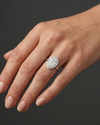A close-up, editorial-style photograph of a woman's elegantly posed hand resting against a seamless dark charcoal gray background. On her ring finger, she wears a white metal engagement ring featuring a large pear-shaped center diamond surrounded by a diamond halo on a split-shank band. The point of the pear-shaped diamond is oriented downward, pointing toward her wrist. Soft, diffused studio lighting highlights the realistic texture of her skin and the brilliant, sparkling facets of the gemstone and metal.