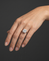 A close-up of a woman's gracefully posed hand wearing a large, princess-cut diamond halo ring against a dark charcoal gray background.